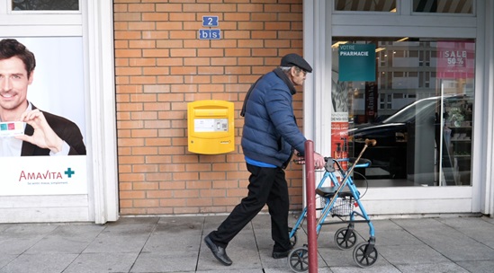 A man walking down a street with shops using his rollator