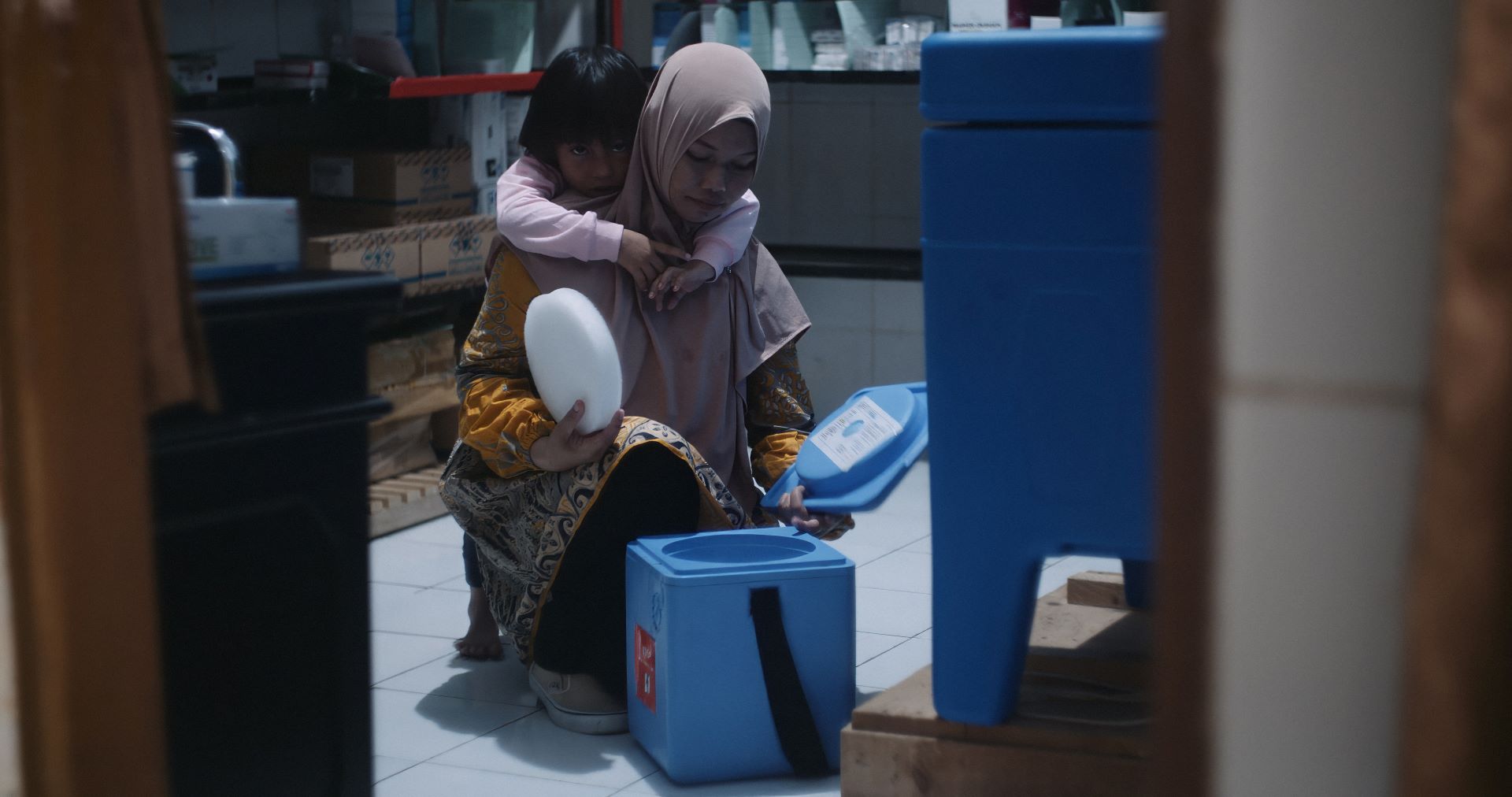 Midwife-Rahmi-prepares-vaccines-Pangkep-Indonesia Midwife Rahmi (Mimi) prepares vaccines at Baring Primary Health Care Centre in Pangkep, Indonesia, for transport to a remote island, while her daughter watches.