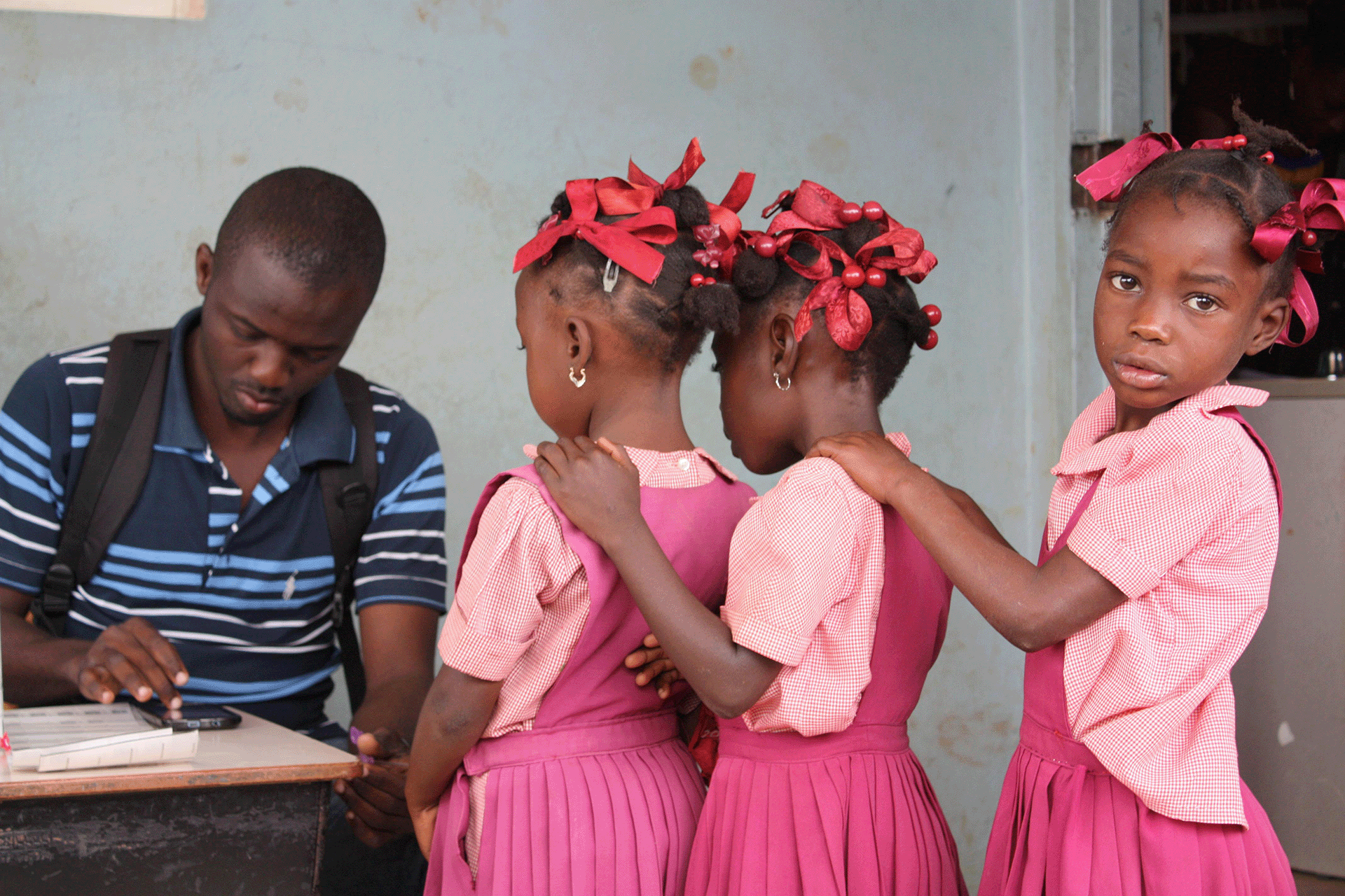 Young girls stand in line in front of a desk where a man sits inputting data into a smartphone