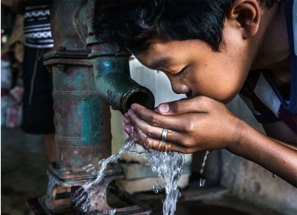 A boy is drinking water from a tap