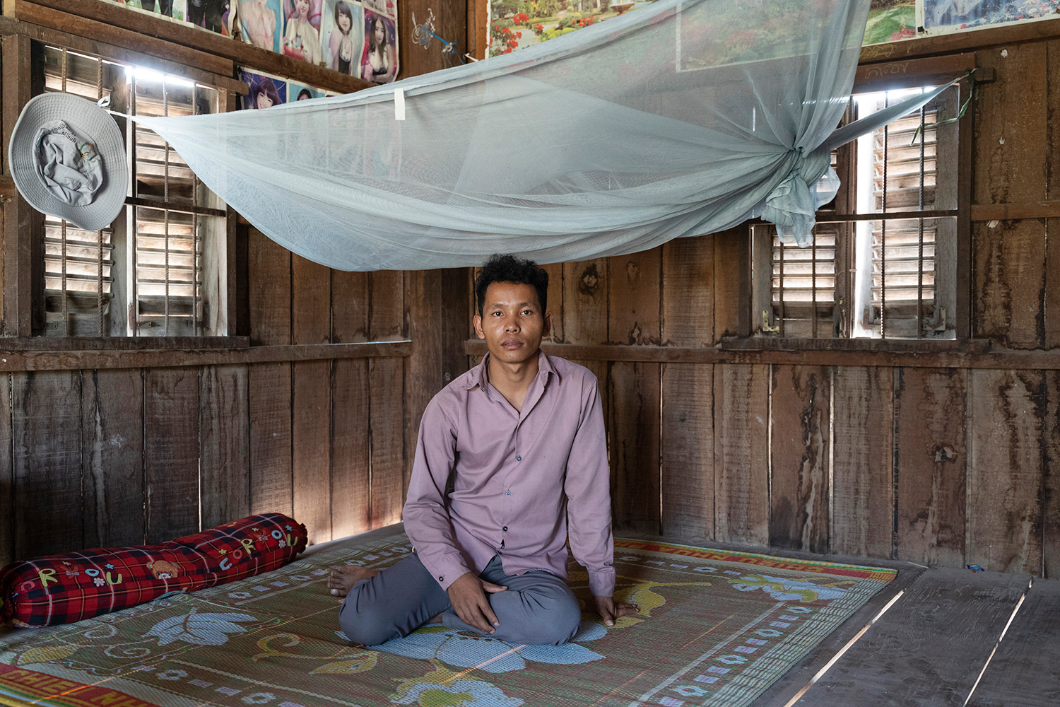 Young man sits under a mosquito net in his house.