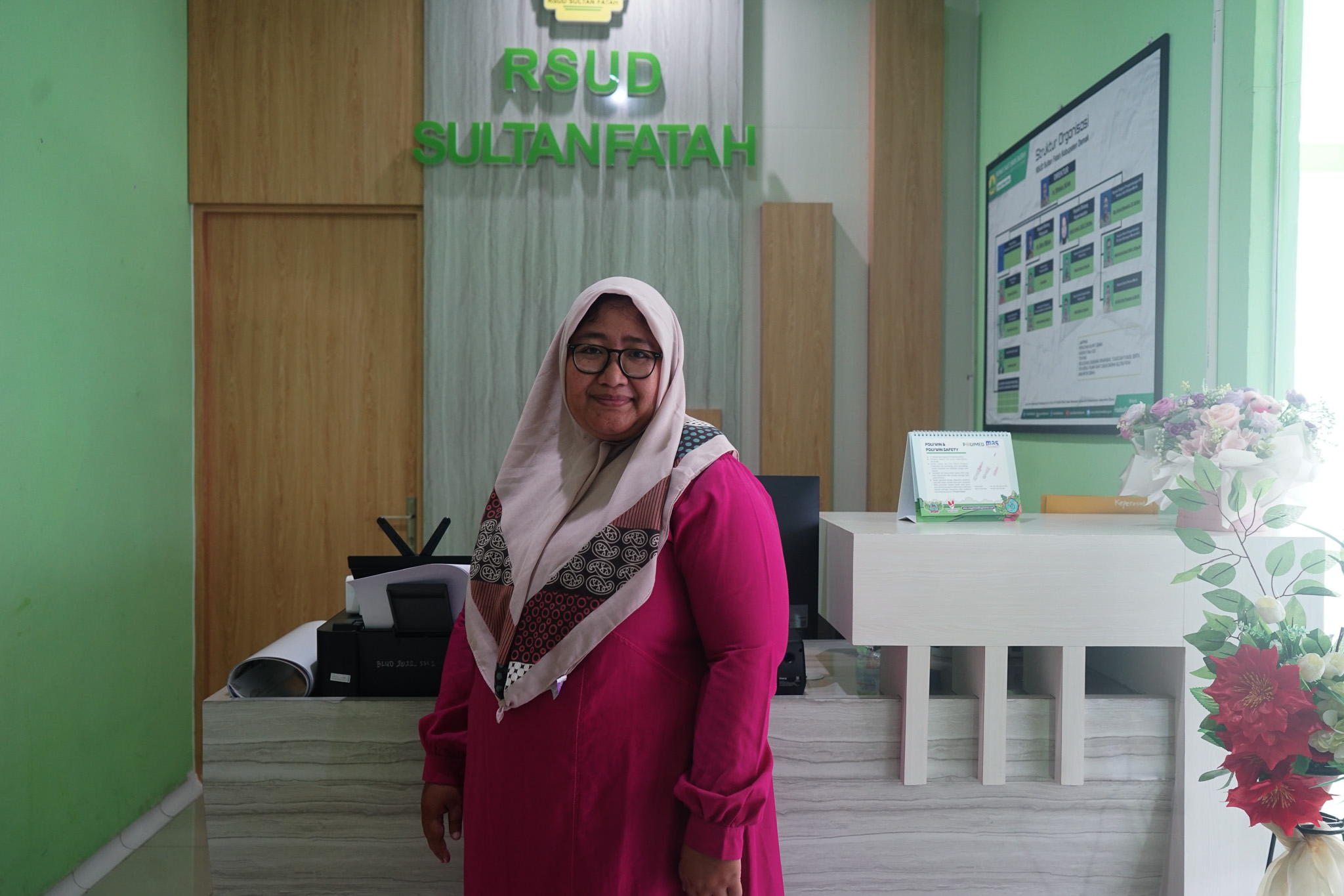 A person wearing a magenta dress and patterned shawl stands in an office setting with the text 