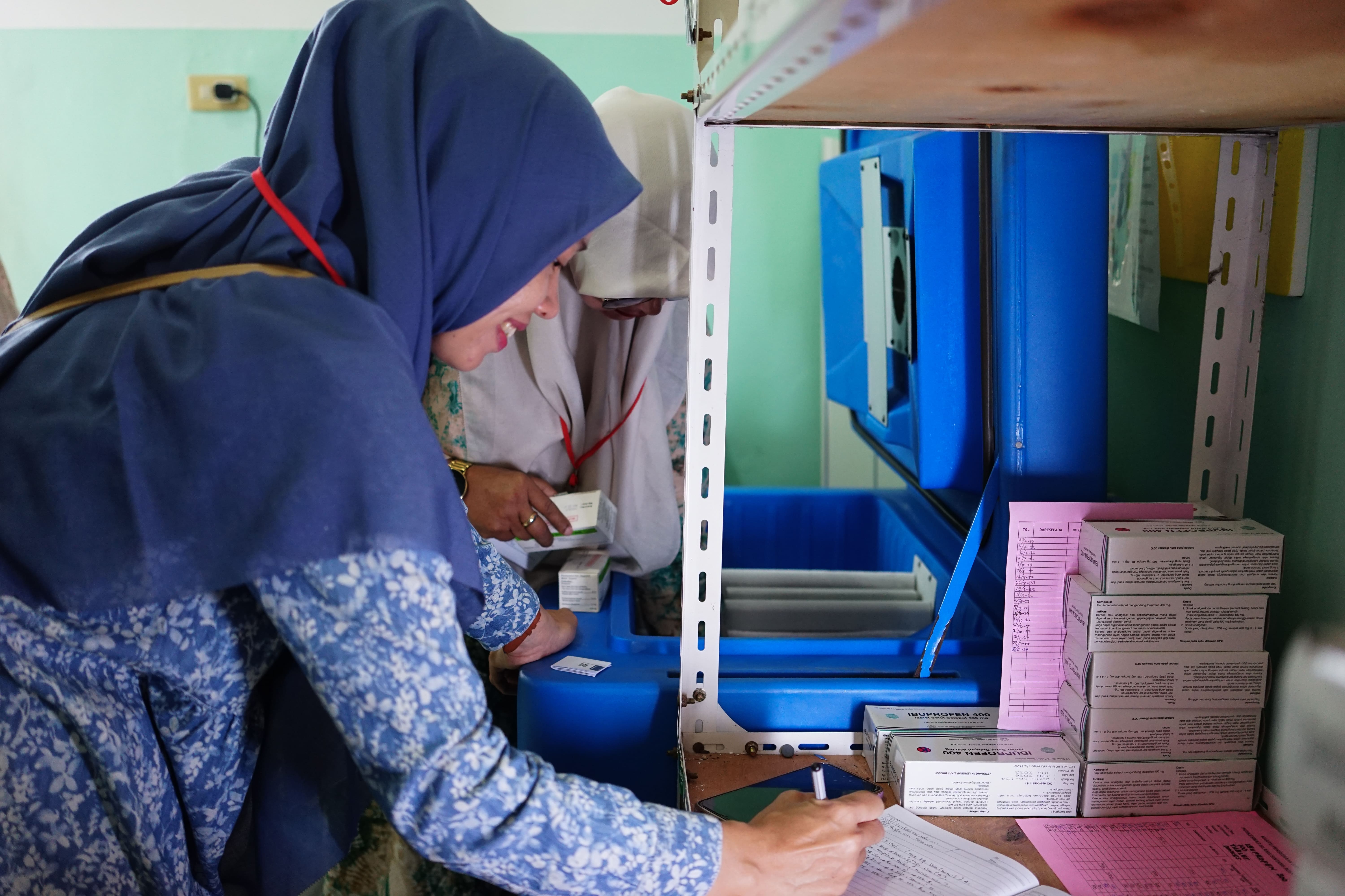 Two women in a health facility carefully checking and organizing vaccine supplies in a cold storage unit.