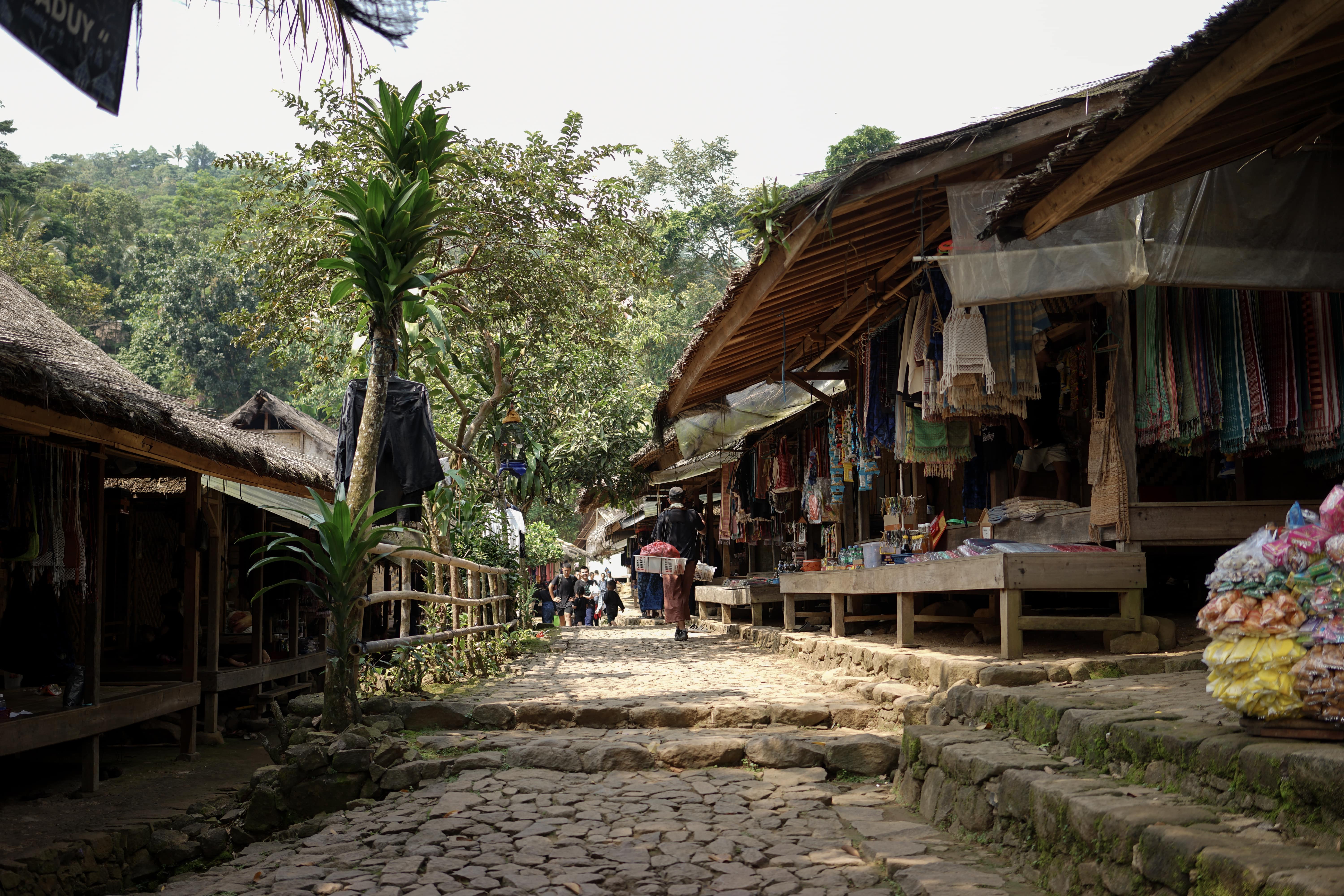 Pemandangan jalan berbatu di desa tradisional dengan rumah-rumah beratap jerami dan kayu.