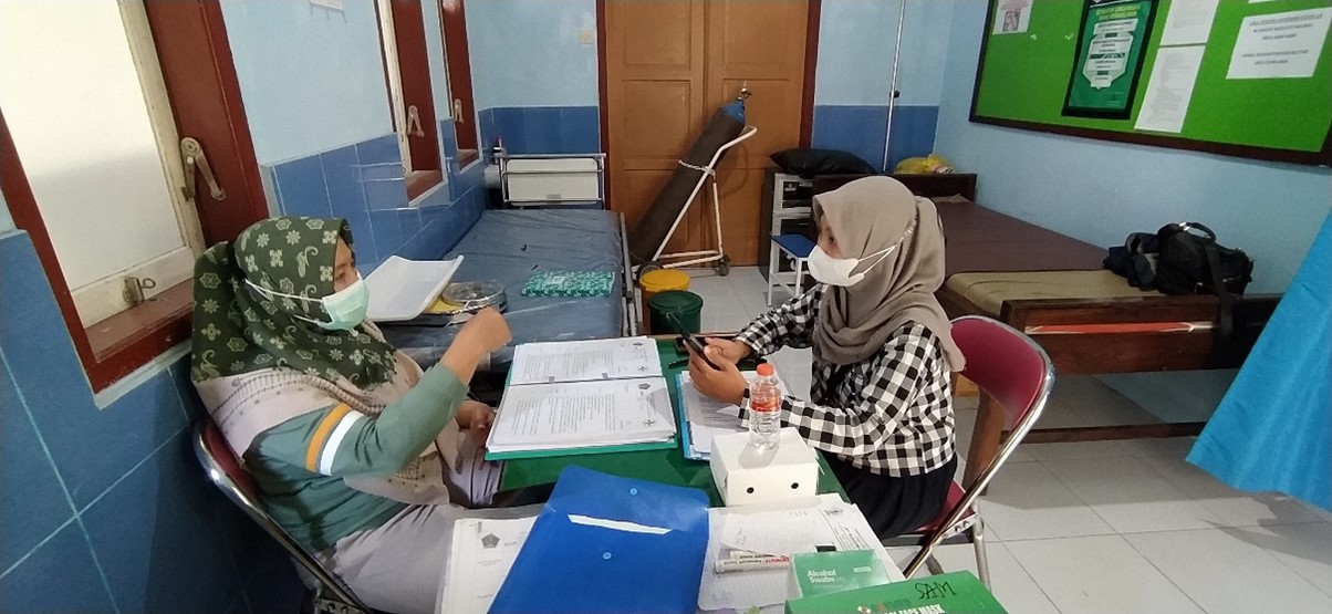 Seorang tenaga kesehatan dan seorang asesor berdiskusi dalam kajian di Puskesmas di Blitar.