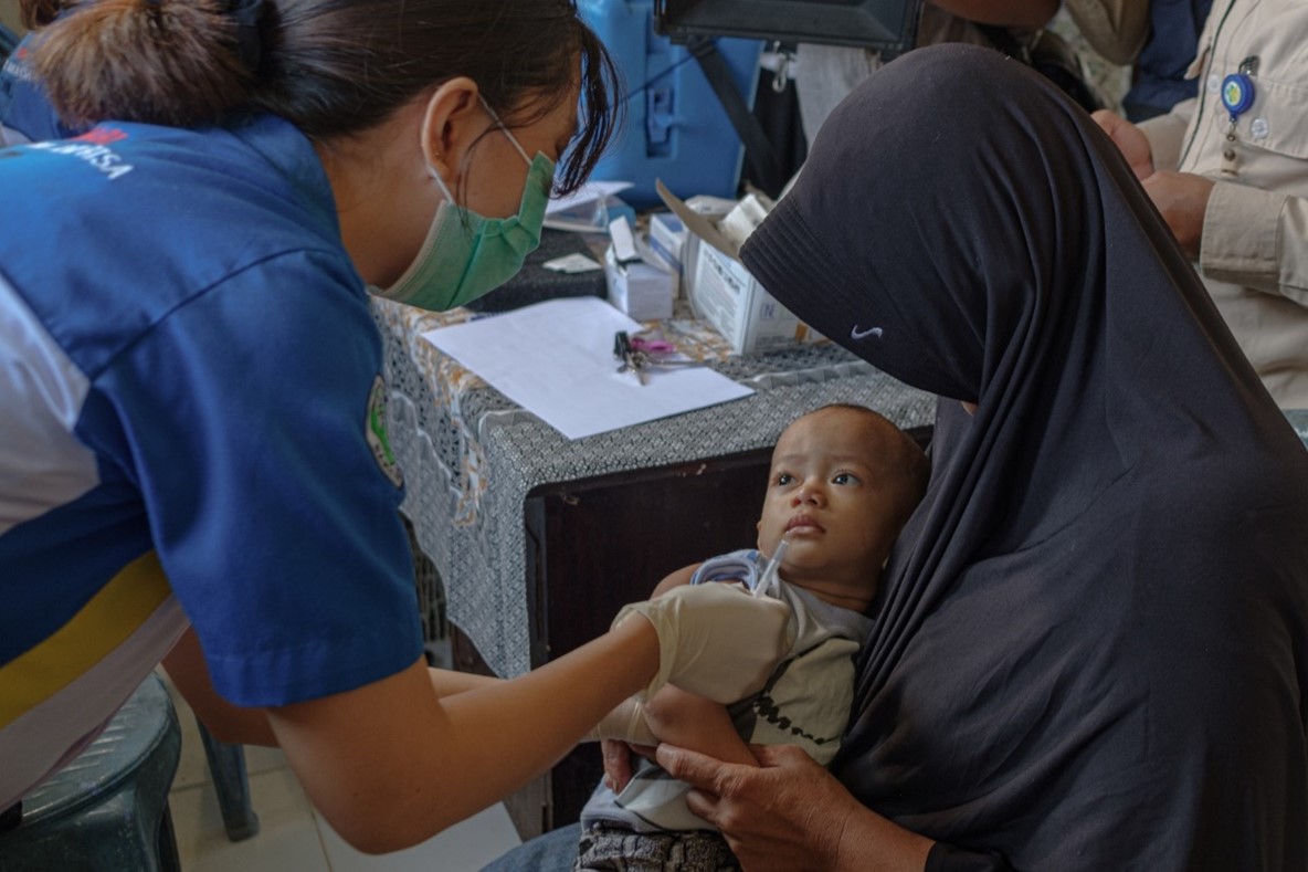 Seorang tenaga kesehatan menyiapkan imunisasi untuk bayi yang digendong neneknya.