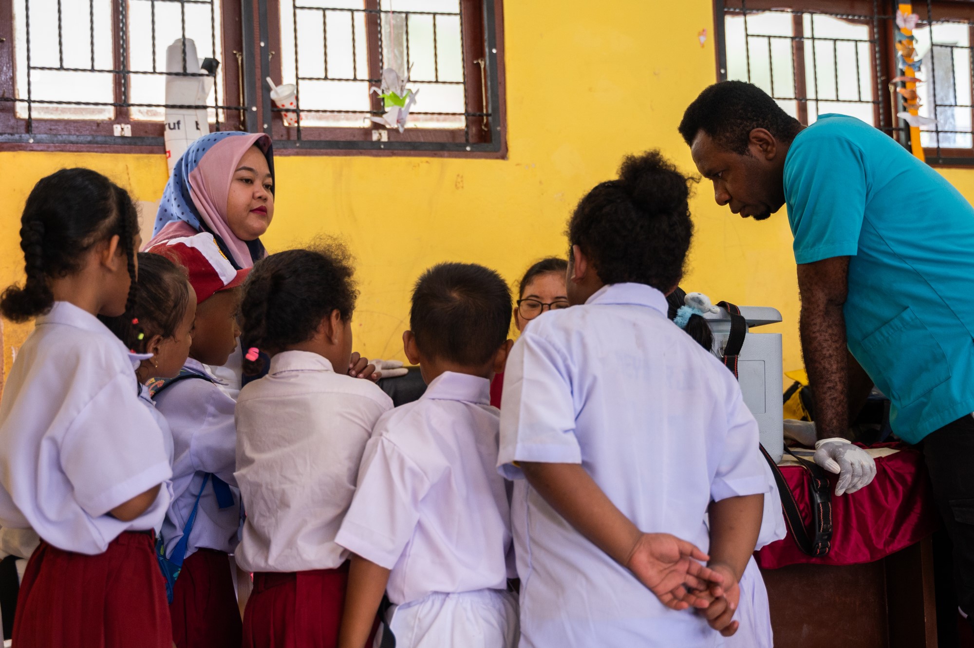 Sekelompok murid Sekolah Dasar berkumpul mengelilingi tenaga kesehatan yang sedang menyiapkan imunisasi polio.