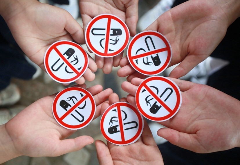 tobaccowebstory2 A group of hands holding red and white circular stickers with a prohibited symbol over a black and white drawing of a cigarette.