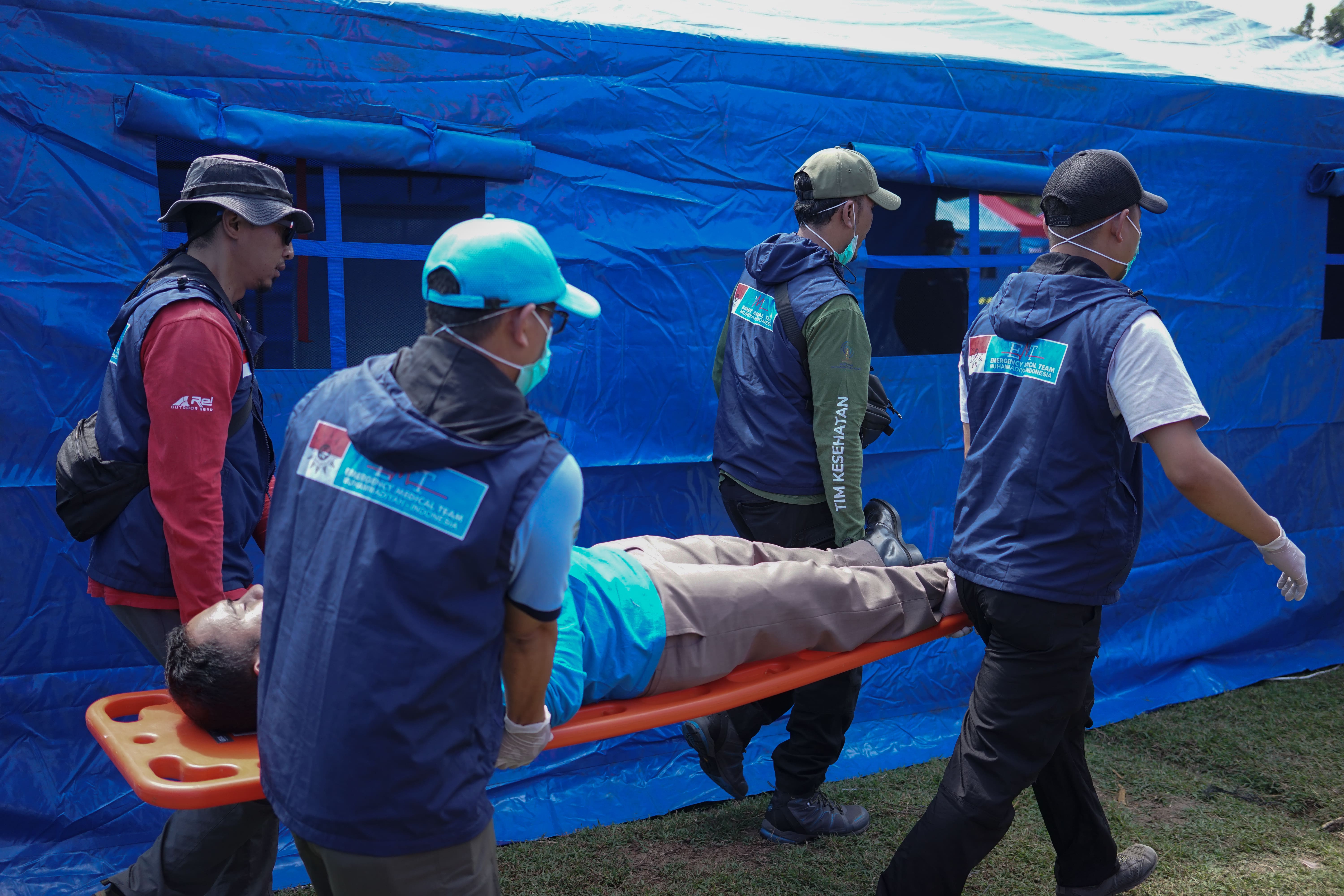 Petugas medis mengevakuasi pasien dengan tandu di area tenda darurat biru.